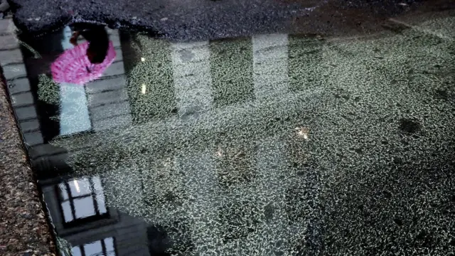 El reflejo de una persona con un paraguas caminando frente a un edificio sobre una charco de agua